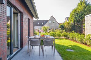 Un patio con mesa para dos, mobiliario exterior y vistas a una zona residencial con casas y vegetación.