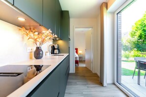 Een moderne keuken met een donkergroene achterwand, een wit aanrechtblad en een vaas met gedroogde bloemen. Er staat een koffiezetapparaat op het aanrecht.