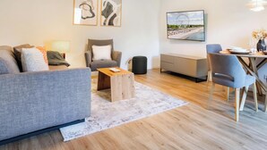 A modern living room with a grey sofa, a wooden coffee table, and a dining area with a table and chairs. - Wind Force 7 - Sea State. Sauna. Patio. Dog-Friendly (Grömitz)