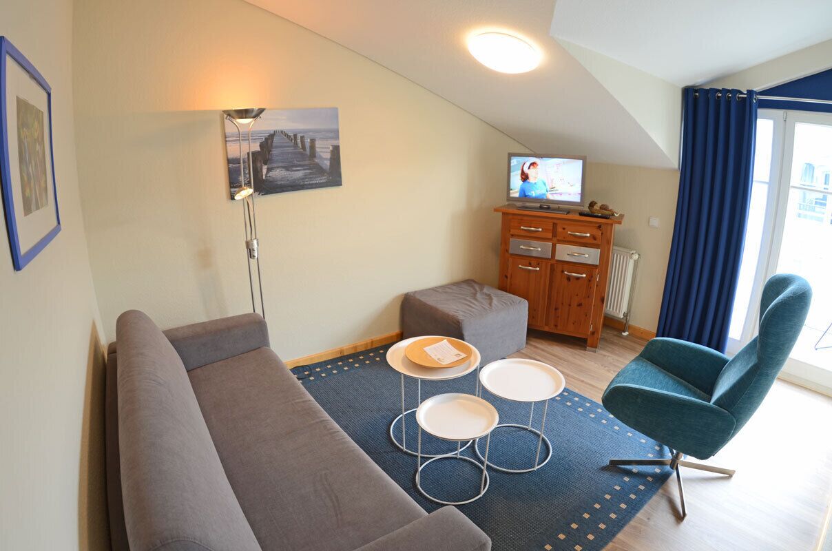 Ein Wohnzimmer mit einer Couch, einem Fernseher, einem Holzkabinett und einem blauen Sessel.