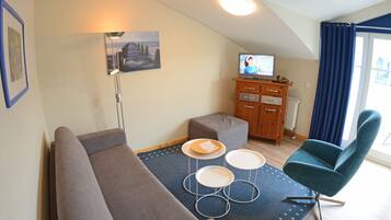 Ein Wohnzimmer mit einer Couch, einem Fernseher, einem Holzkabinett und einem blauen Sessel.
