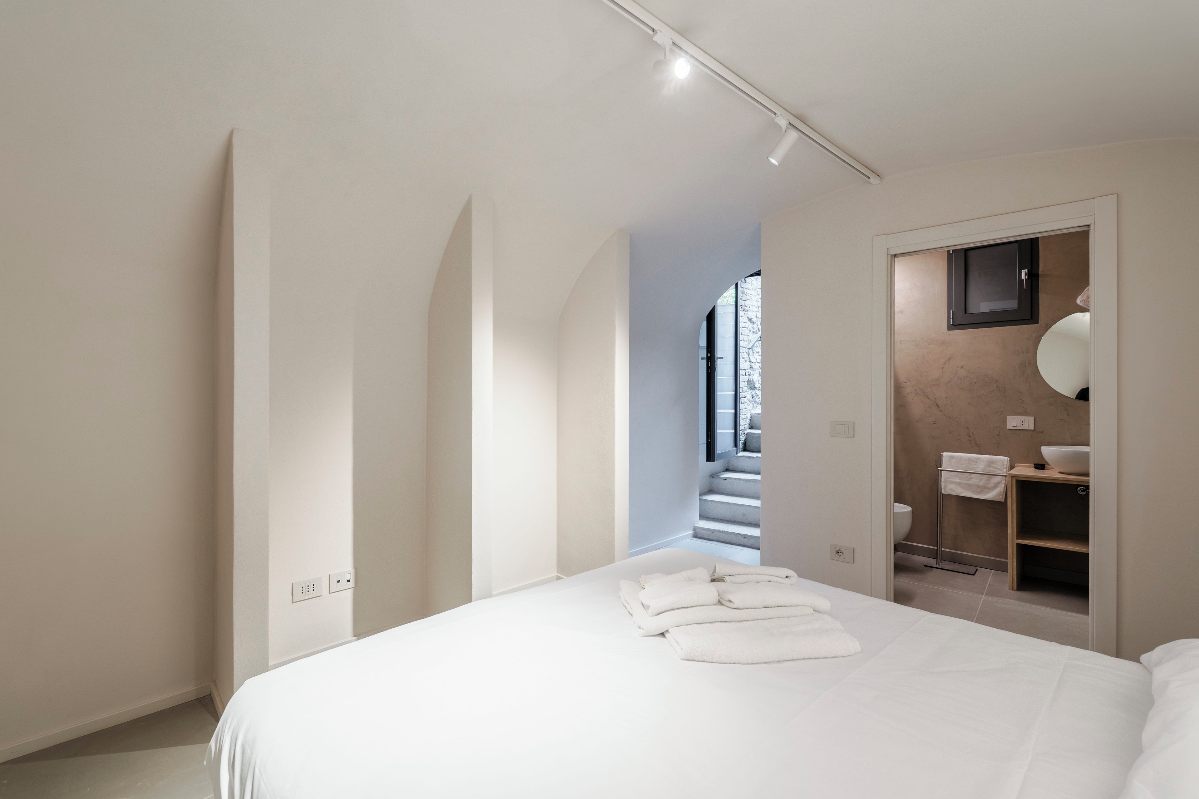 A modern bedroom with a large bed, a bathroom with a marble countertop, and a view of a staircase.