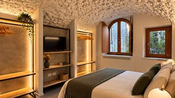 A bedroom with a stone ceiling, a bed with pillows, a bedside table with a lamp, and a TV on a stand.