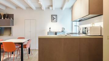 Een moderne keuken met een centraal eiland, een eetgedeelte met een tafel en stoelen, en een wit plafond met zichtbare balken.