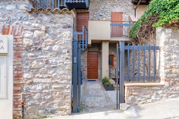 A stone building with a gated entrance, a small garden, and a staircase leading to a wooden door. - Residenza Cittadella (Lonato del Garda)