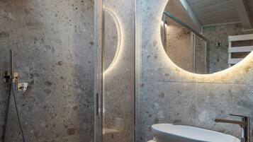 A modern bathroom with a stone wall, a glass shower enclosure, and a round mirror with integrated lighting.