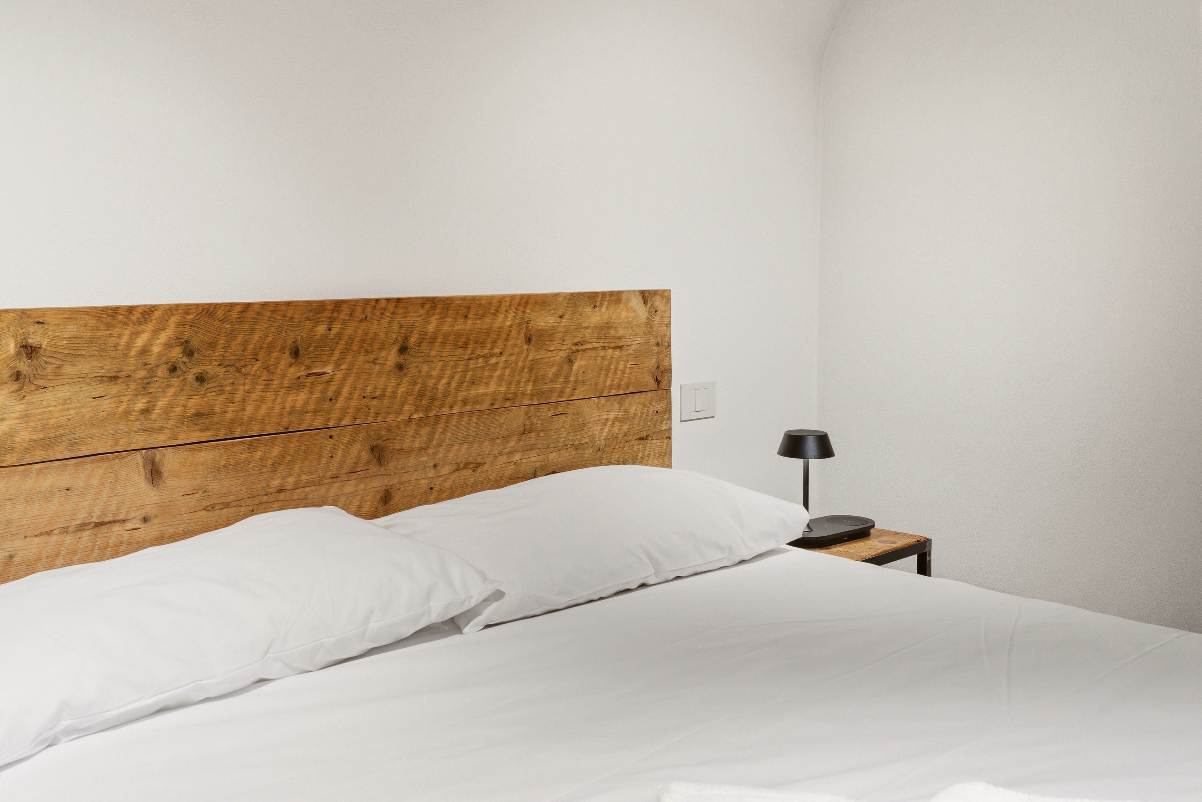 Un lit avec une tête de lit en bois, une literie blanche et une petite table de chevet avec une lampe.