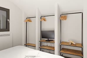 A hotel room with a bed, a desk with a computer, and a wardrobe with hanging clothes. - Residenza Cittadella (Lonato del Garda)