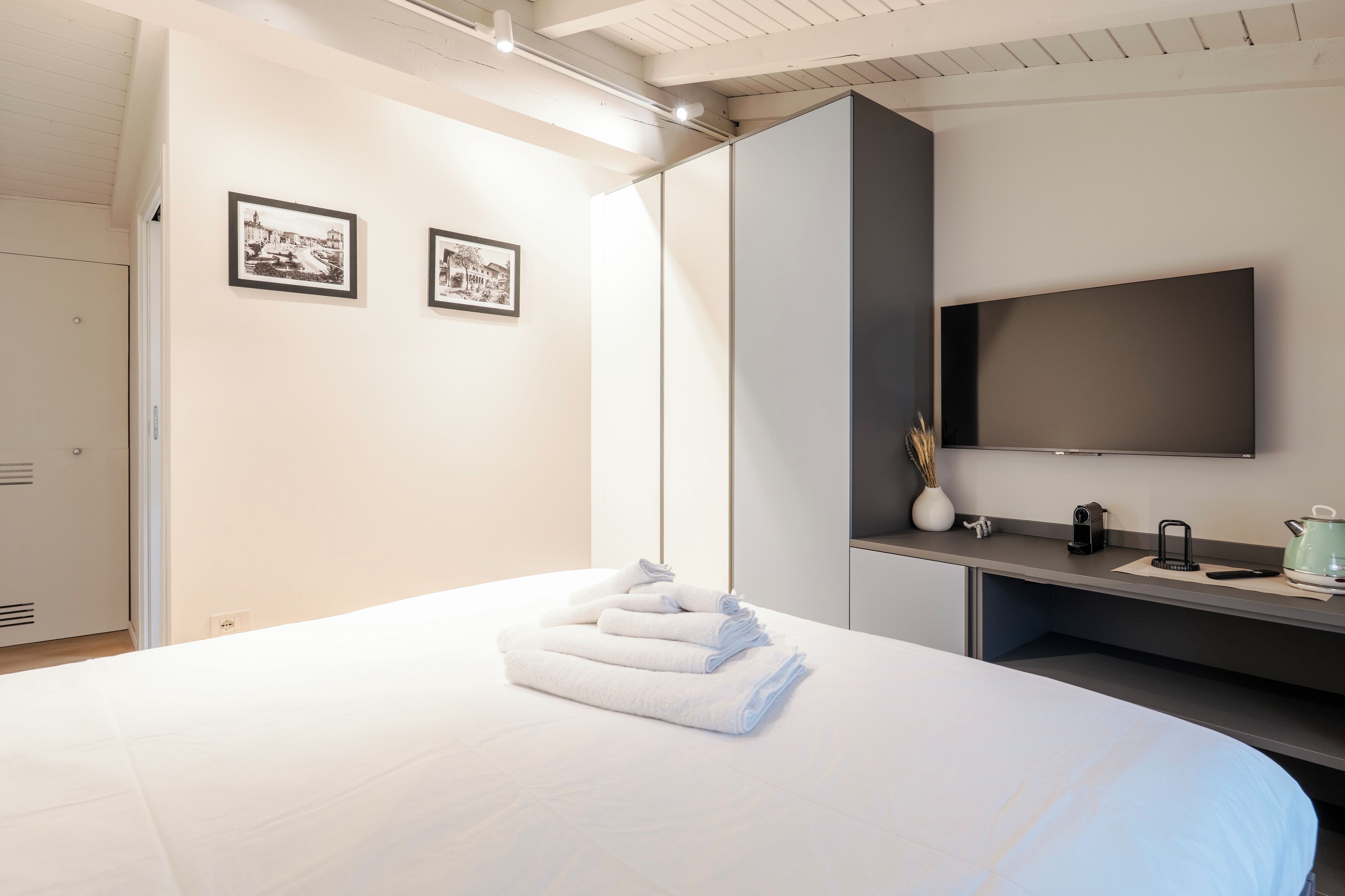 Una habitación de hotel con una cama, un televisor de pantalla plana montado en la pared y dos cuadros enmarcados.