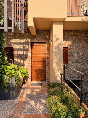 Une façade en pierre avec une porte en bois, un escalier en métal et un jardinier avec des plantes vertes.