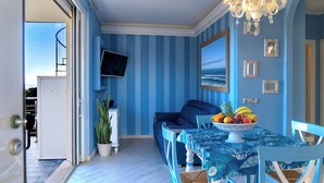 Ein Zimmer mit blauen Streifen an der Wand, einem Sofa, einem Esstisch mit Obstschale und einem an der Wand befestigten Fernseher.