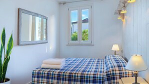 Ein Zimmer mit einem Bett, einem Nachttisch mit Lampe, einem Fenster mit Blick auf Grünflächen und einem Spiegel an der Wand.