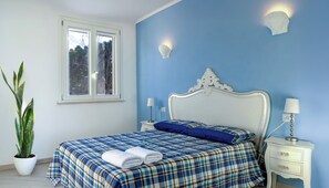 A bedroom with a bed, bedside tables, a lamp, a wall-mounted light, a window, and a potted plant. - BLUE OCEAN-VIEW APARTMENT, terrace, air conditioning, internet, and parking space (San Vincenzo)