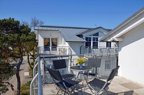 A balcony with outdoor seating, a railing, and a view of a building with a white facade and a window with yellow curtains. - Juliusruh Seaside Resort, 2nd floor, town center, quiet location, right on the sandy beach (Juliusruh)