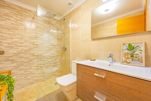 Ein modernes Badezimmer mit Duschkabine aus Glas, einer weißen Toilette, einem hölzernen Waschtisch mit Spiegel und einem gerahmten Bild an der Wand.