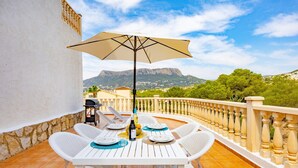 A terrace with a table and chairs, an umbrella, and a view of mountains. - Hanami Apartment - Plusholidays (Calpe / Calp)