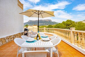 A terrace with a table and chairs, an umbrella, and a view of mountains. - Hanami Apartment - Plusholidays (Calpe / Calp)