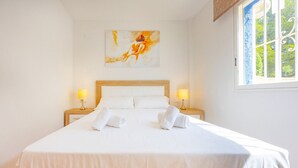 A hotel room with a large bed, two bedside lamps, a painting on the wall, and a window with a view of greenery. - Hanami Apartment - Plusholidays (Calpe / Calp)