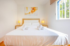A hotel room with a large bed, two bedside lamps, a painting on the wall, and a window with a view of greenery. - Hanami Apartment - Plusholidays (Calpe / Calp)