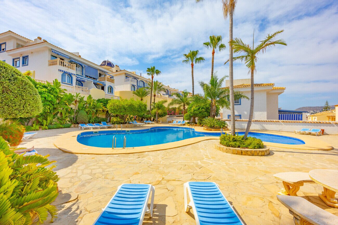 A pool area with lounge chairs, palm trees, and a building with blue accents.