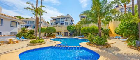 A swimming pool with a curved edge, surrounded by palm trees and lounge chairs.