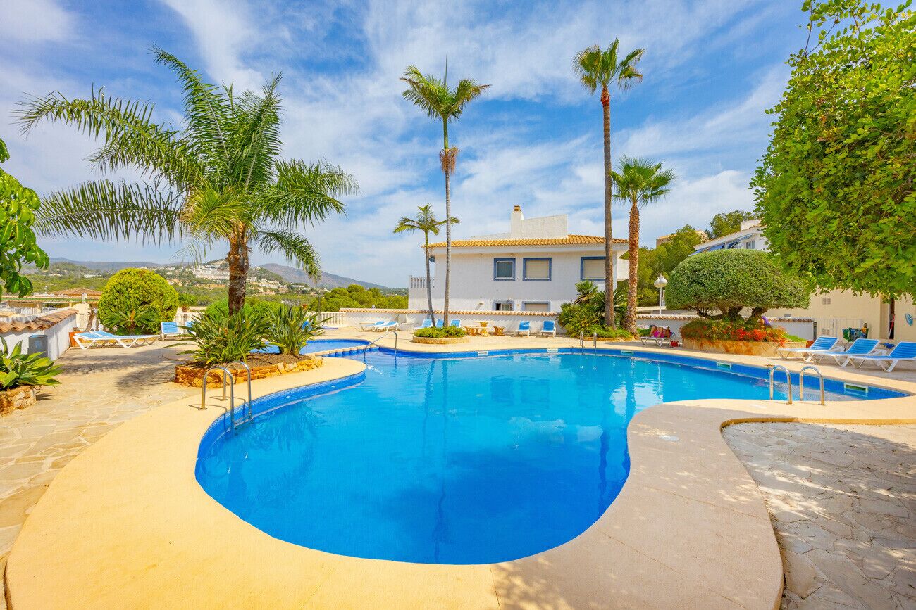 A swimming pool with a curved edge, surrounded by lounge chairs and palm trees, with a building in the background.