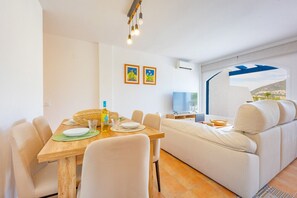 Ein modernes Wohnzimmer mit Essbereich, einer Couch, einem Fernseher und einem großen Fenster mit Ausblick.