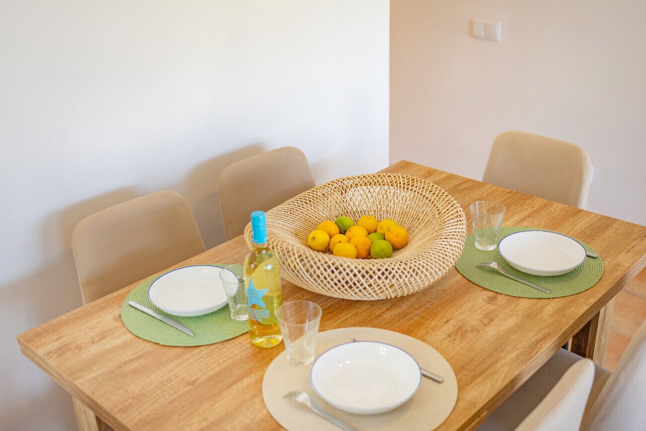 A dining table set with plates, cutlery, a glass, a bottle, and a basket of lemons.