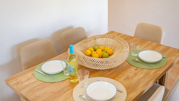 A dining table set with plates, cutlery, a glass, a bottle, and a basket of lemons. - Hanami Apartment - Plusholidays (Calpe / Calp)