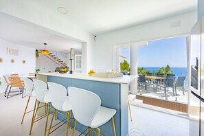 A modern kitchen with a bar area, a staircase, and a balcony with a view of the sea. - Villa Infinitysea - PlusHolidays (Altea)