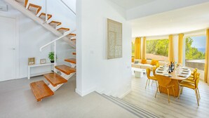 Ein modernes Interieur mit einer Treppe, einem Essbereich und Blick durch große Fenster.