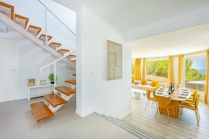 Ein modernes Interieur mit einer Treppe, einem Essbereich und Blick durch große Fenster.