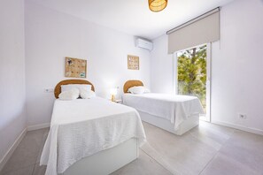 A bedroom with two beds, a window with a view of trees, and a wall-mounted air conditioner. - Villa Infinitysea - PlusHolidays (Altea)