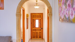 Um corredor com porta de madeira, um candelabro e um quadro na parede.