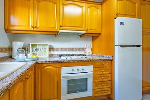 A kitchen with wooden cabinets, a white refrigerator, a stove, and a microwave. - Calasanz Apartment - Plusholidays (Calpe / Calp)