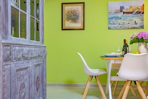 A dining area with a table set for two, a white chair, and a cabinet with glass doors. - Calasanz Apartment - Plusholidays (Calpe / Calp)