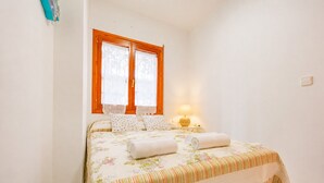 Um quarto com cama, almofadas, mesa de cabeceira, luminária e janela com cortinas.