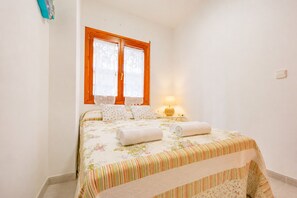 A bedroom with a bed, pillows, a nightstand, a lamp, and a window with curtains. - Calasanz Apartment - Plusholidays (Calpe / Calp)