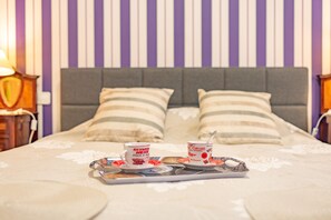 A neatly made bed with a tray of breakfast items including two mugs and a teapot, set against a striped wallpaper background. - Calasanz Apartment - Plusholidays (Calpe / Calp)