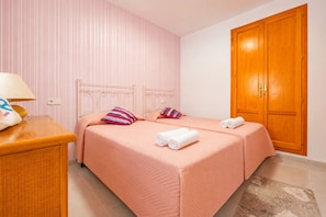 A hotel room with two beds, a wooden wardrobe, a bedside table with a lamp, and a striped wall. - Calasanz Apartment - Plusholidays (Calpe / Calp)