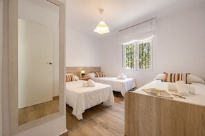 A hotel room with two beds, a wooden desk, a window with curtains, and a hanging light fixture. - Villa Lacampana - Plusholidays (Calpe / Calp)