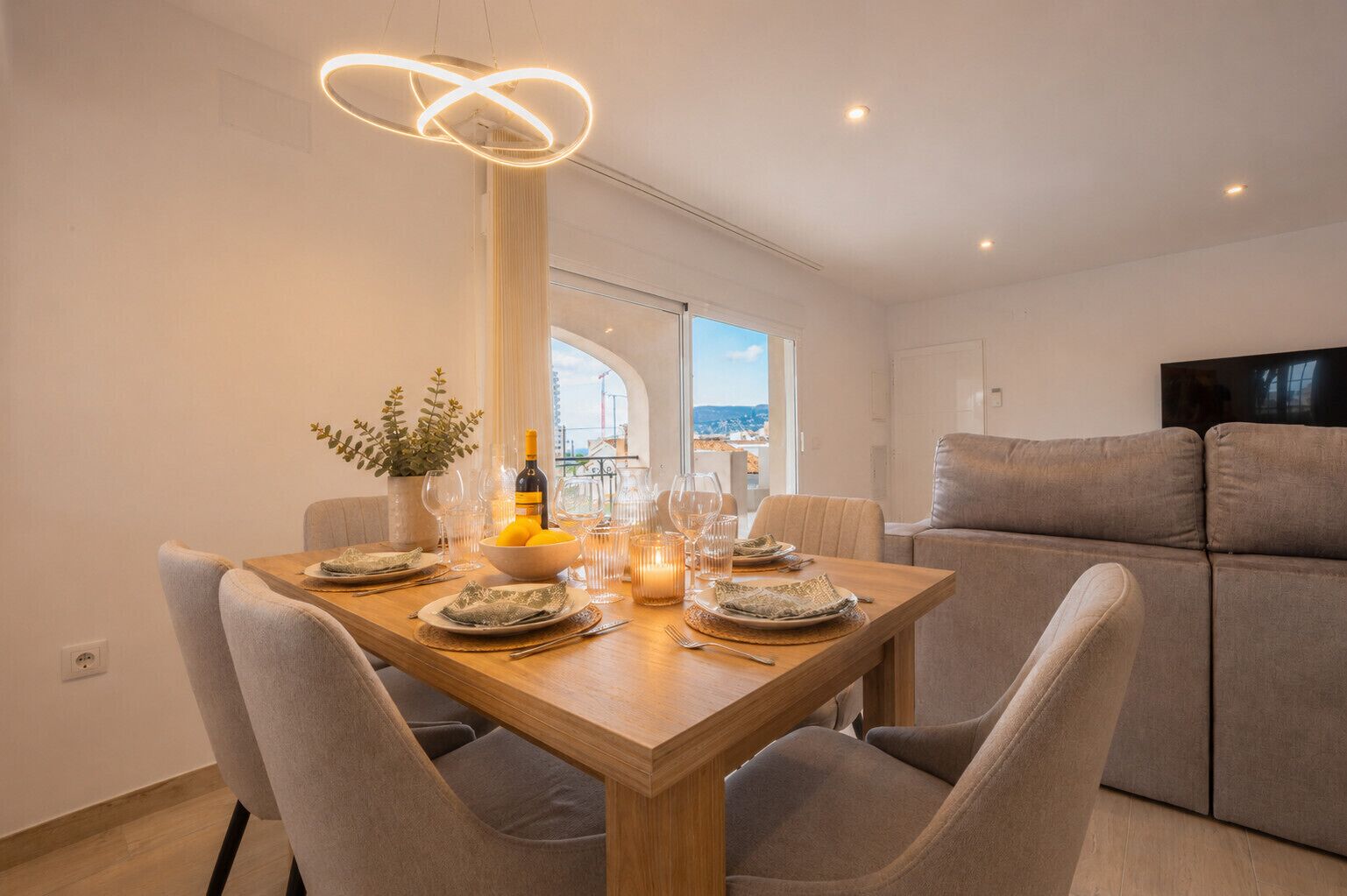 Un coin repas avec une table en bois dressée pour quatre personnes, entourée de chaises à revêtement gris.
