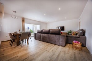 A modern living room with a brown sofa, a dining table with chairs, and a TV mounted on the wall. - Villa Lacampana - Plusholidays (Calpe / Calp)