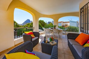A balcony with wicker furniture, a table, and chairs, overlooking a cityscape with a mountain in the distance. - Villa Lacampana - Plusholidays (Calpe / Calp)