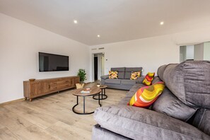 A modern living room with a grey sofa, a wooden cabinet, a flat-screen TV, and a small coffee table. - Villa Lacampana - Plusholidays (Calpe / Calp)