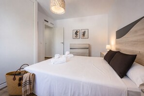 A neatly made bed with white linens and two pillows, a bedside lamp, and a woven basket with a blanket. - Villa Lacampana - Plusholidays (Calpe / Calp)