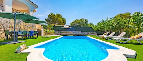 Ein Swimmingpool mit einer Steinsäule und einer Rasenfläche mit Liegestühlen.