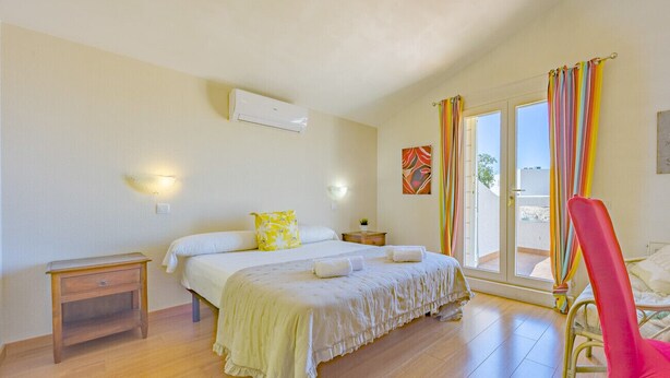 A bedroom with a bed, bedside tables, a chair, and a window with curtains. - Villa Descanso - Plusholidays (Calpe / Calp)