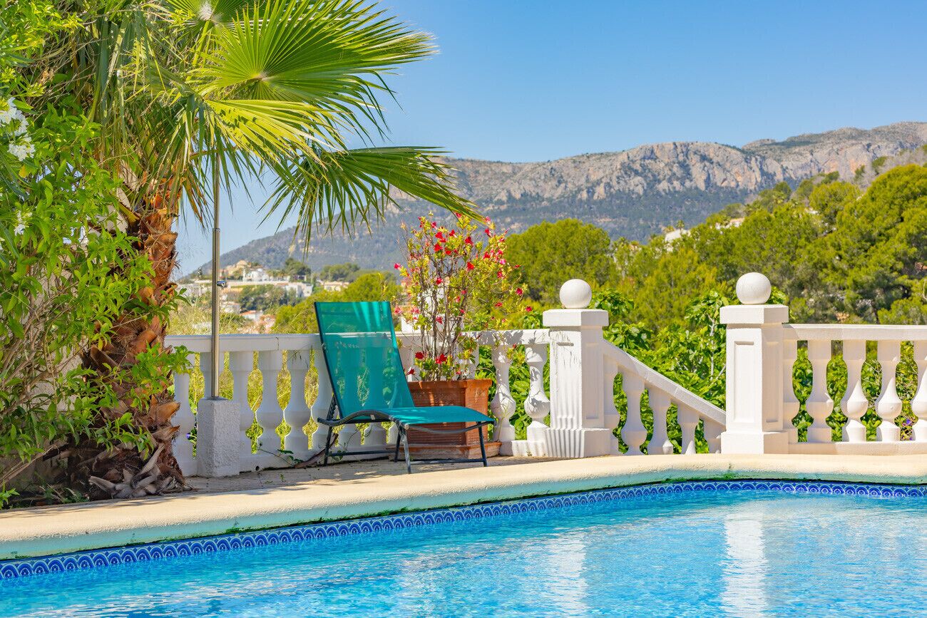 A swimming pool with a white balustrade, a green lounge chair, and a potted plant with red flowers.