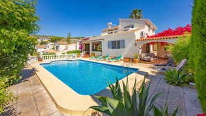 A pool area with a clear blue pool, lounge chairs, and a white building with a balcony. - Villa Descanso - Plusholidays (Calpe / Calp)
